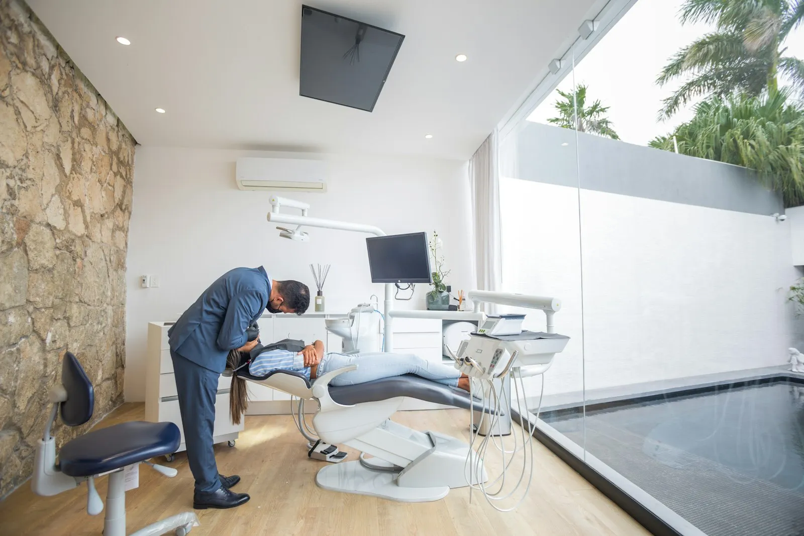 A dentist leaning over a seated patient in a bright dental office.