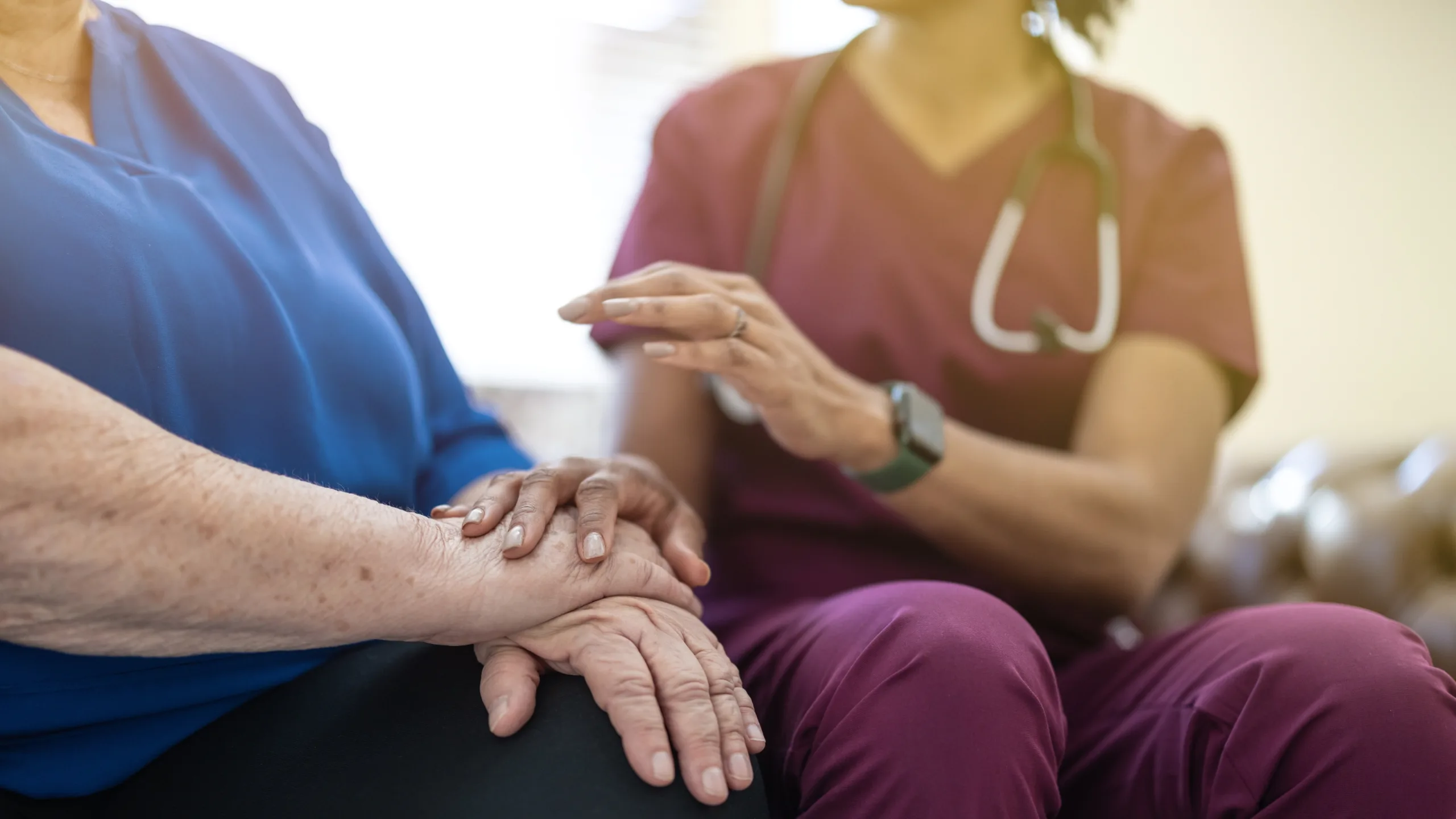 A nurse holding the hands of an elderly patient in a calm clinical setting